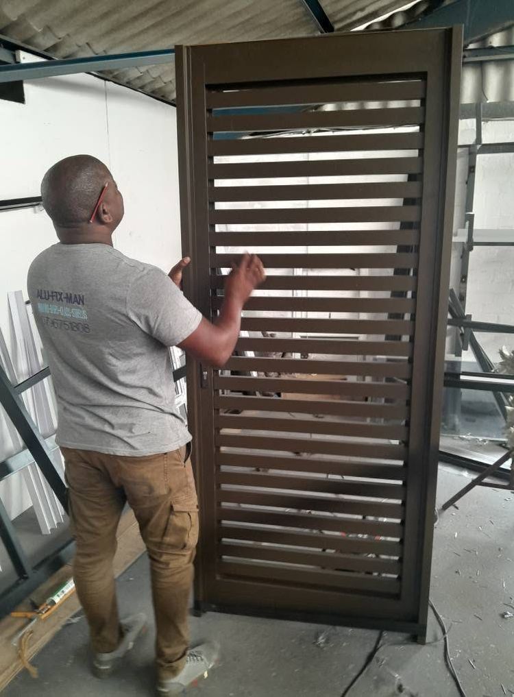 An installer with a bronze slatted aluminium gate in the workshop