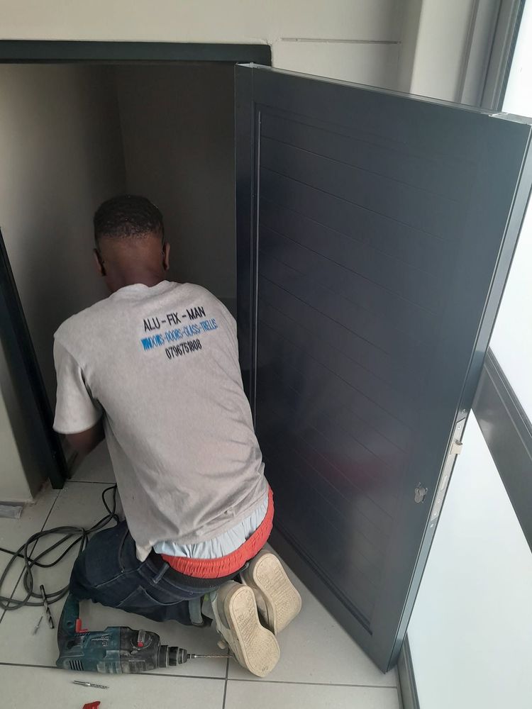 An Alufixman installer fitting a charcoal aluminium door indoors