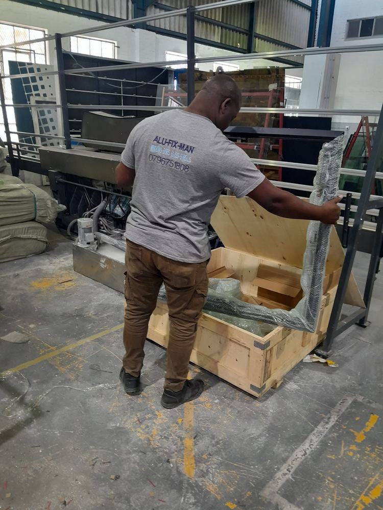 An installer lifting a wrapped aluminium frame from its crate in the workshop