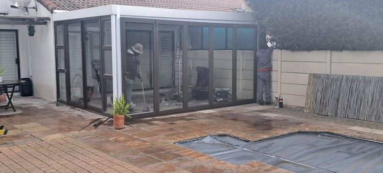 A patio closed in with black aluminium and glass beside a pool
