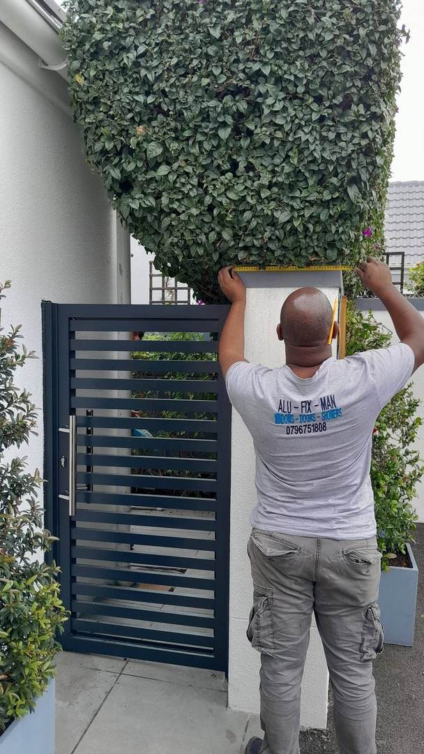 An Alufixman installer measuring a slatted aluminium gate beside a hedge