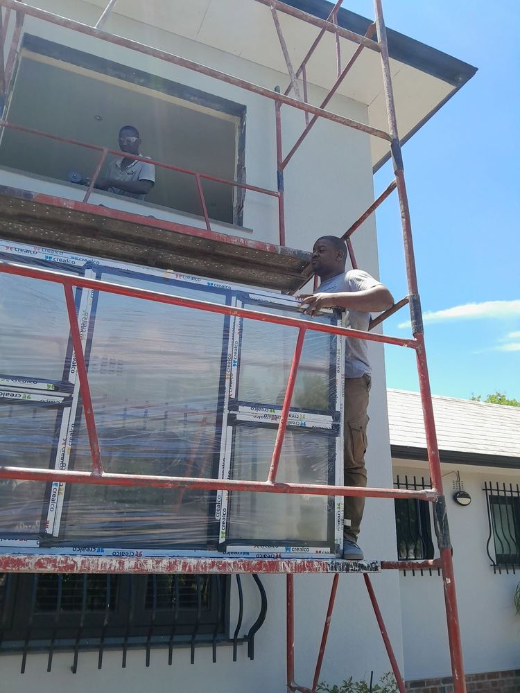 An Alufixman installer on scaffolding fitting windows to a double-storey house